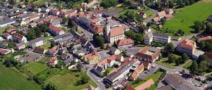 Luftaufnahme einer kleinen Stadt mit vielen Gebäuden und grünen Feldern. Die Stadt ist von Bäumen und Pflanzen umgeben und hat eine Straße in der Mitte.