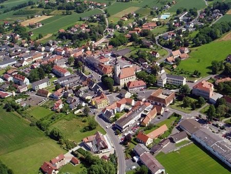 Luftaufnahme einer kleinen Stadt mit vielen Gebäuden und grünen Feldern. Die Stadt ist von Bäumen und Pflanzen umgeben und hat eine Straße in der Mitte.
