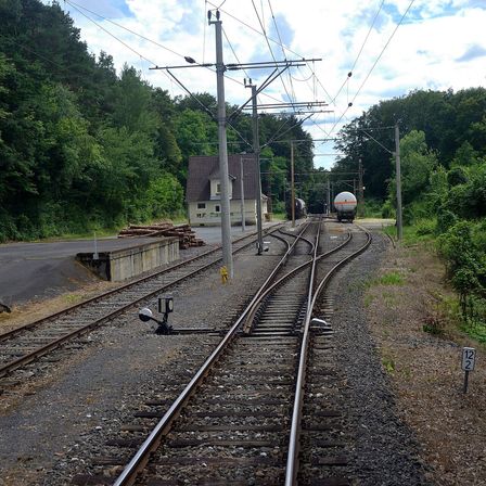 Eine ländliche Eisenbahnszene mit mehreren Gleisen, einem Haus und einem Zug mit einem großen Tankwagen. Die Gleise sind von Grün umgeben.