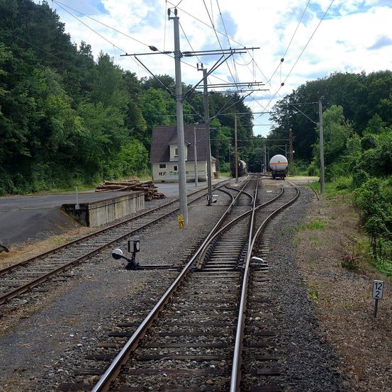 Eine ländliche Eisenbahnszene mit mehreren Gleisen, einem Haus und einem Zug mit einem großen Tankwagen. Die Gleise sind von Grün umgeben.