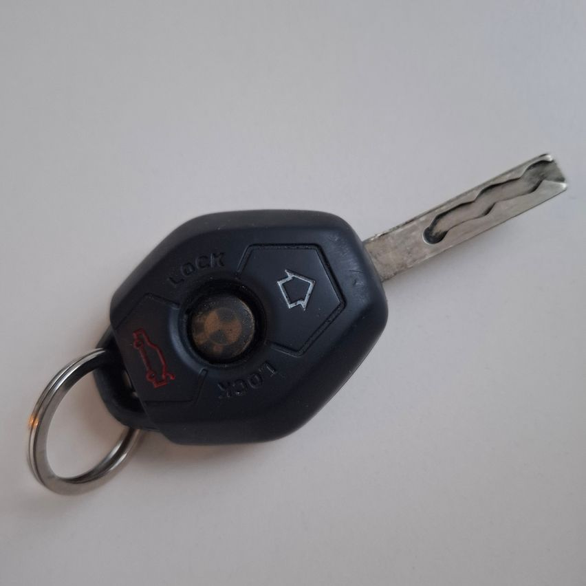 A black car key with a key fob. It has a lock button and a red emblem.