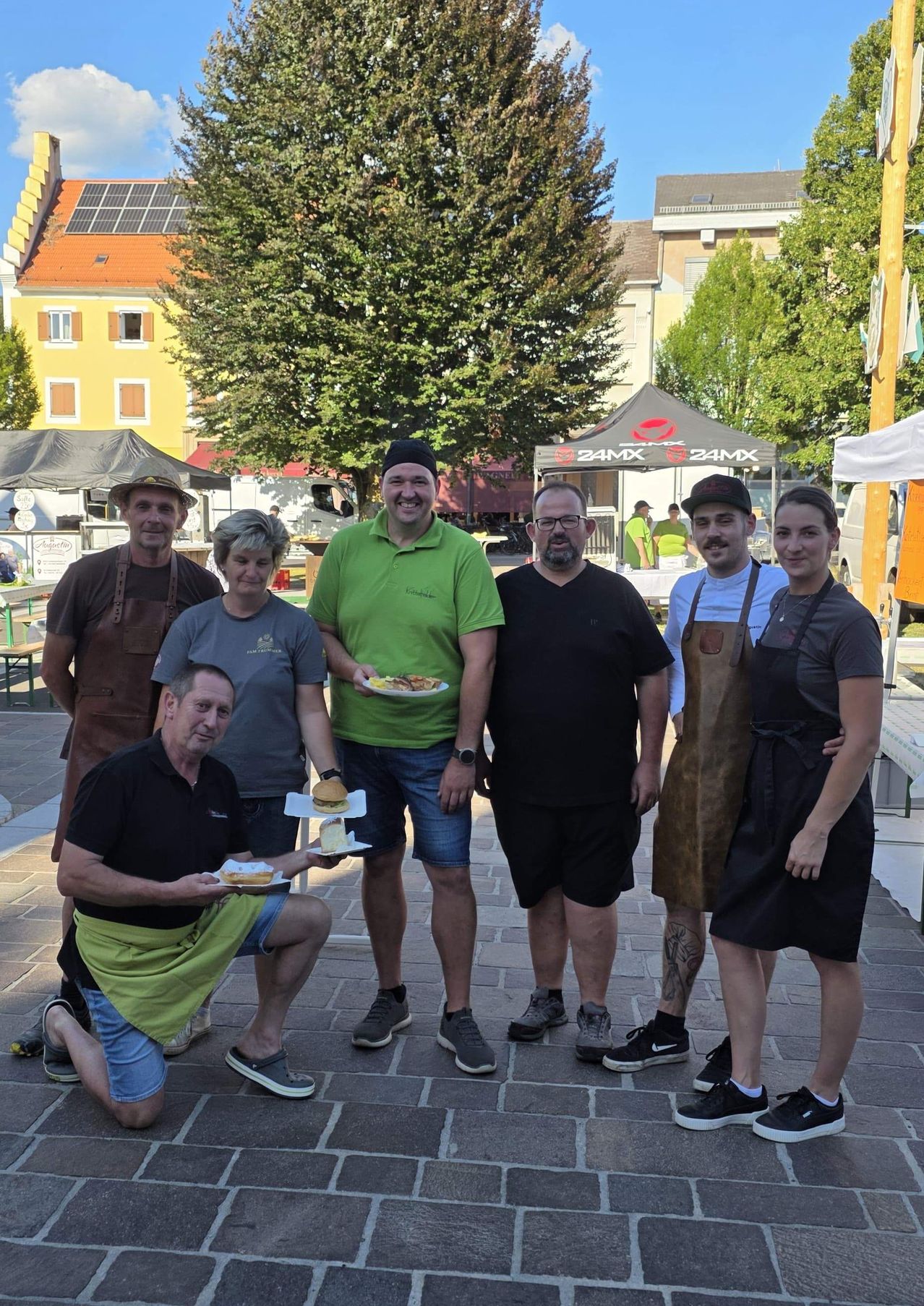 A group of people, possibly a team, stand in front of a building with food. They are smiling and posing for a photo.
