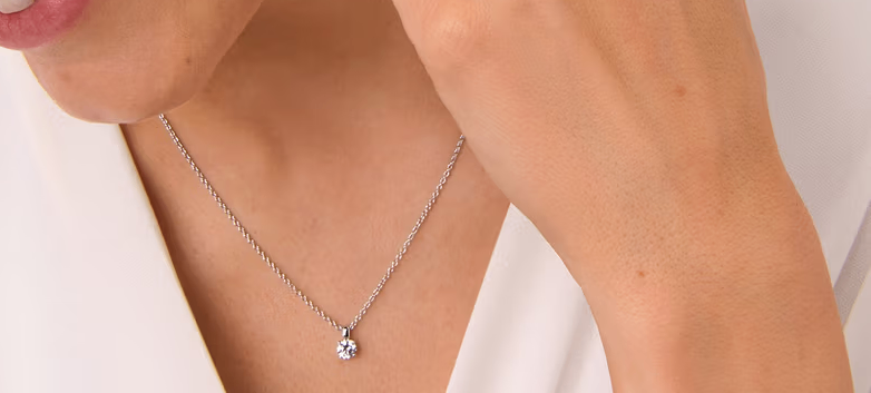 A woman wearing a silver necklace with a small diamond pendant.