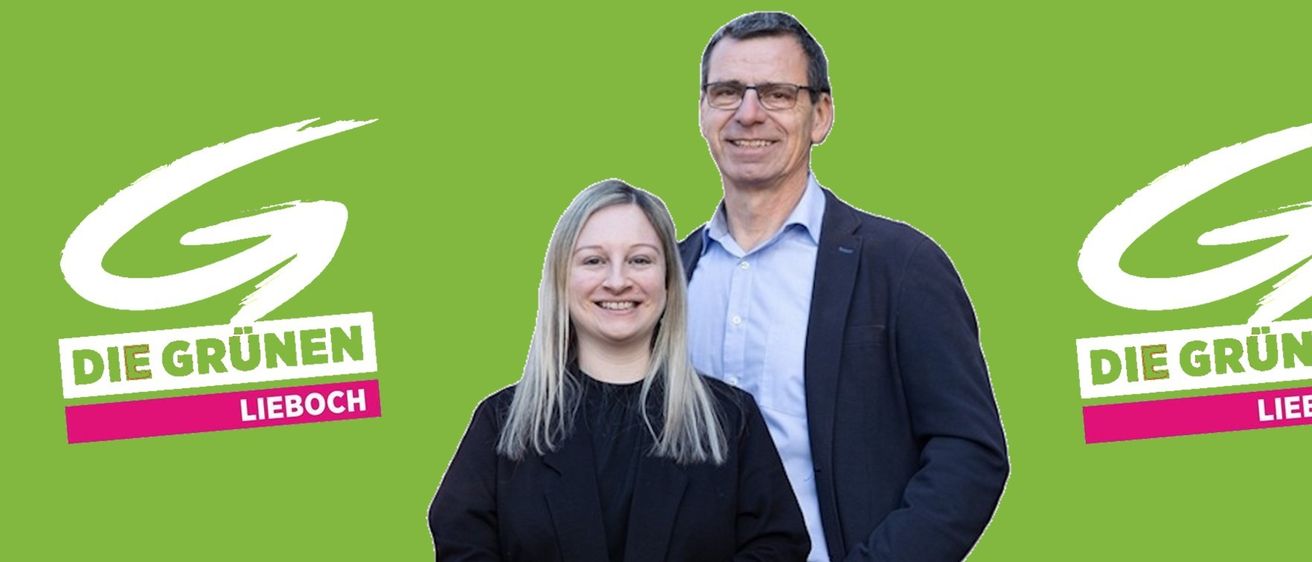 Ein Mann und eine Frau stehen nebeneinander und lächeln beide. Der Mann trägt eine Brille und einen Anzug, und die Frau trägt einen schwarzen Blazer. Sie stehen vor einem grünen Hintergrund.