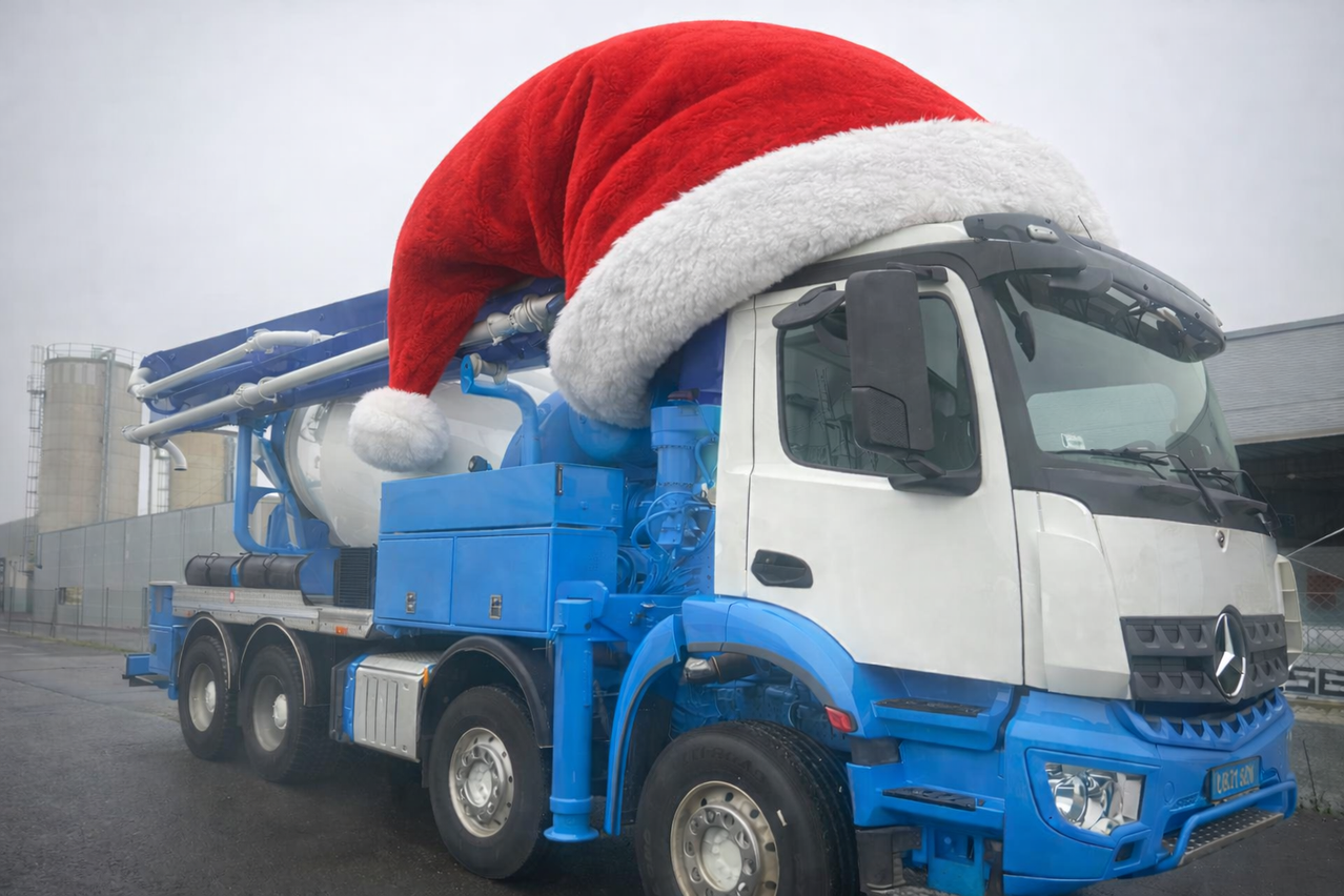 Ein blauer und weißer Lastwagen mit einem roten und weißen Weihnachtsmannhut auf der Oberseite. Der Lastwagen hat einen großen Zementmischer hinten.