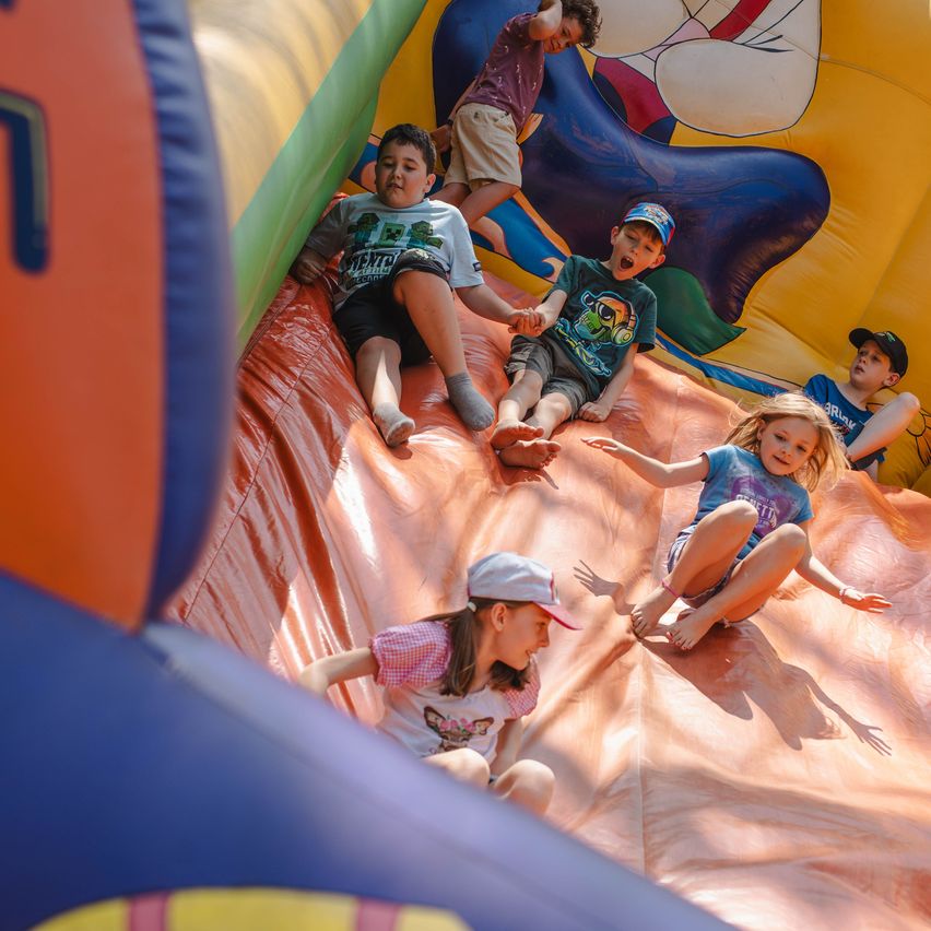 Fünf Kinder spielen in einem aufblasbaren Gleiter, zwei gleiten herunter, zwei sitzen und beobachten, und eines steht im Hintergrund.