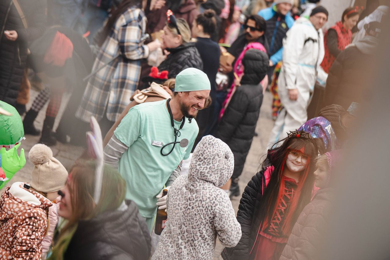 Eine Menschenmenge, darunter ein Arzt und ein Kind in einem Leoparden-Kostüm, lächelt in einer festlichen Atmosphäre.