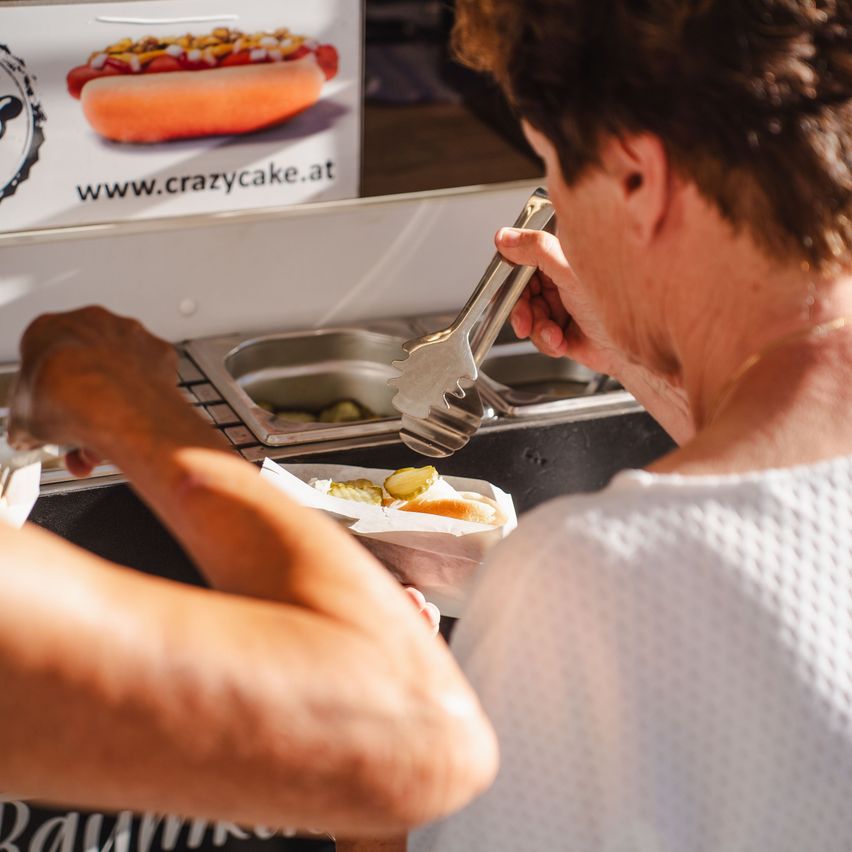 Eine Frau bereitet einen Hot Dog mit Gurken in einem Imbisswagen zu.