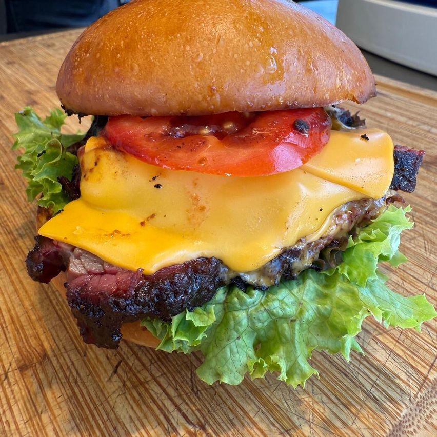 Ein Burger mit zwei Käsescheiben, einer Tomate und Salat auf einer Holzoberfläche. Der Burger ist halbgegessen.