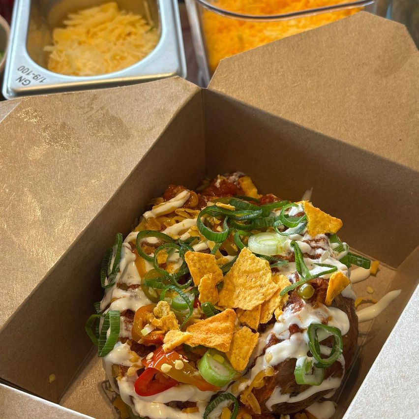 Ein Kartoffelgericht mit Toppings wie saure Sahne, Käse und Tortilla-Chips in einer braunen Box.