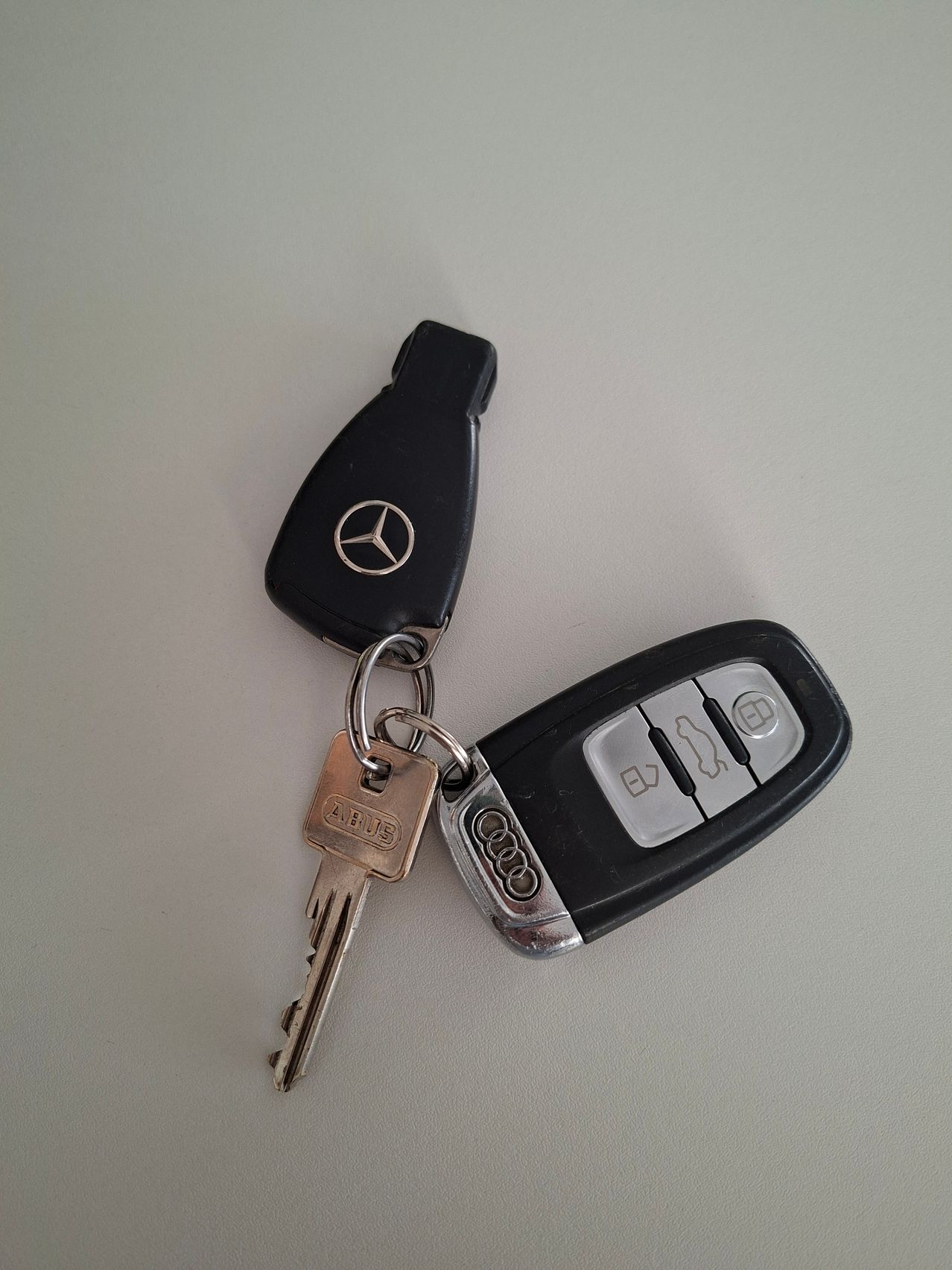A Mercedes-Benz key with a silver key and a black key fob with a silver Audi logo on a white surface.