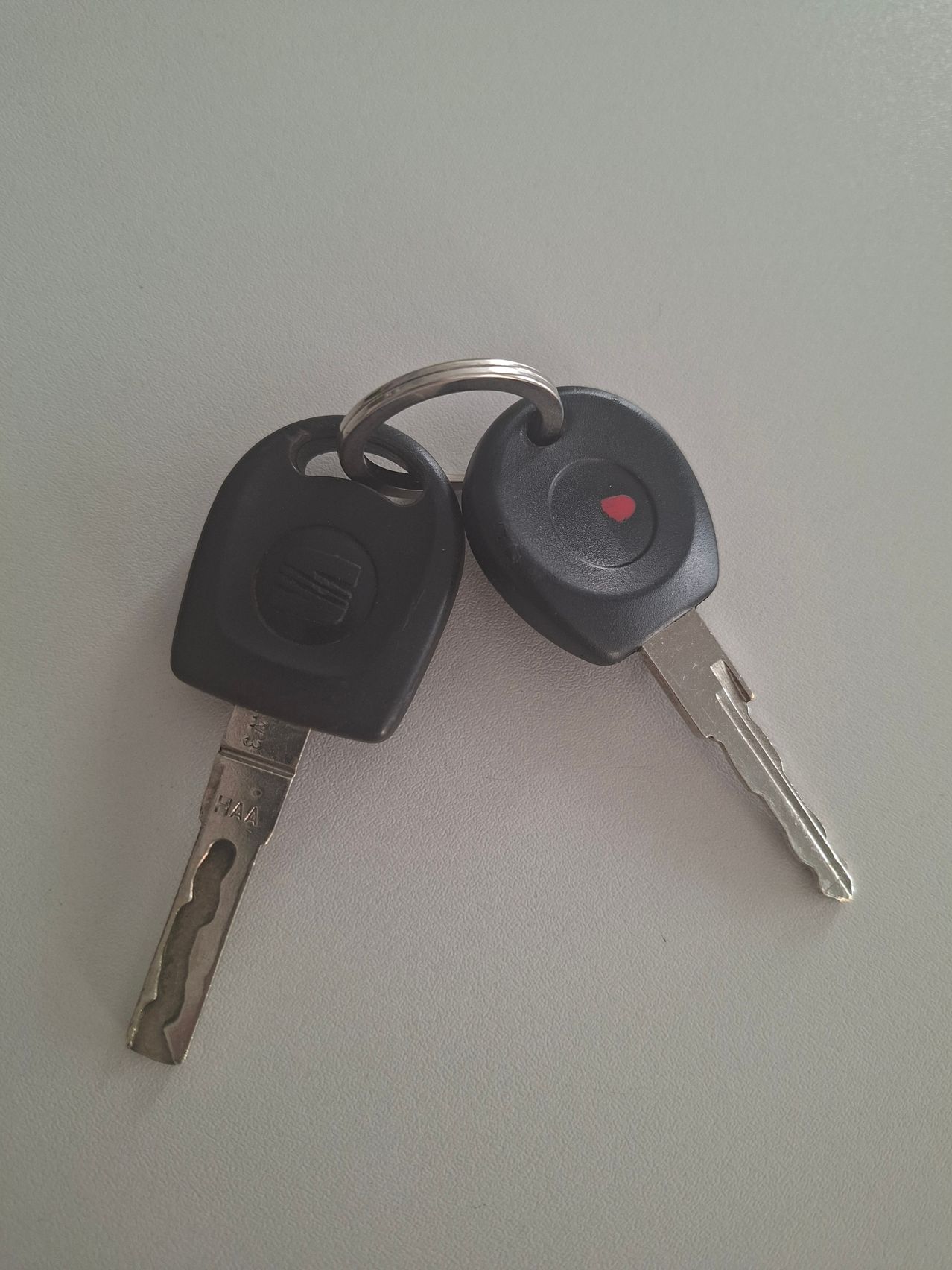 Two black car keys with silver blades and a red dot on one key's keychain.