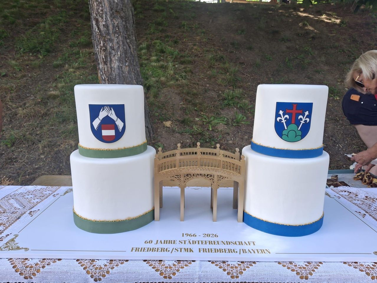 Ein Kuchen mit zwei Türmen, jeder mit einem anderen Wappen. Die Brücke in der Mitte hat Text, der 1966-2026 60 Jahre Städtefreundschaft lautet.