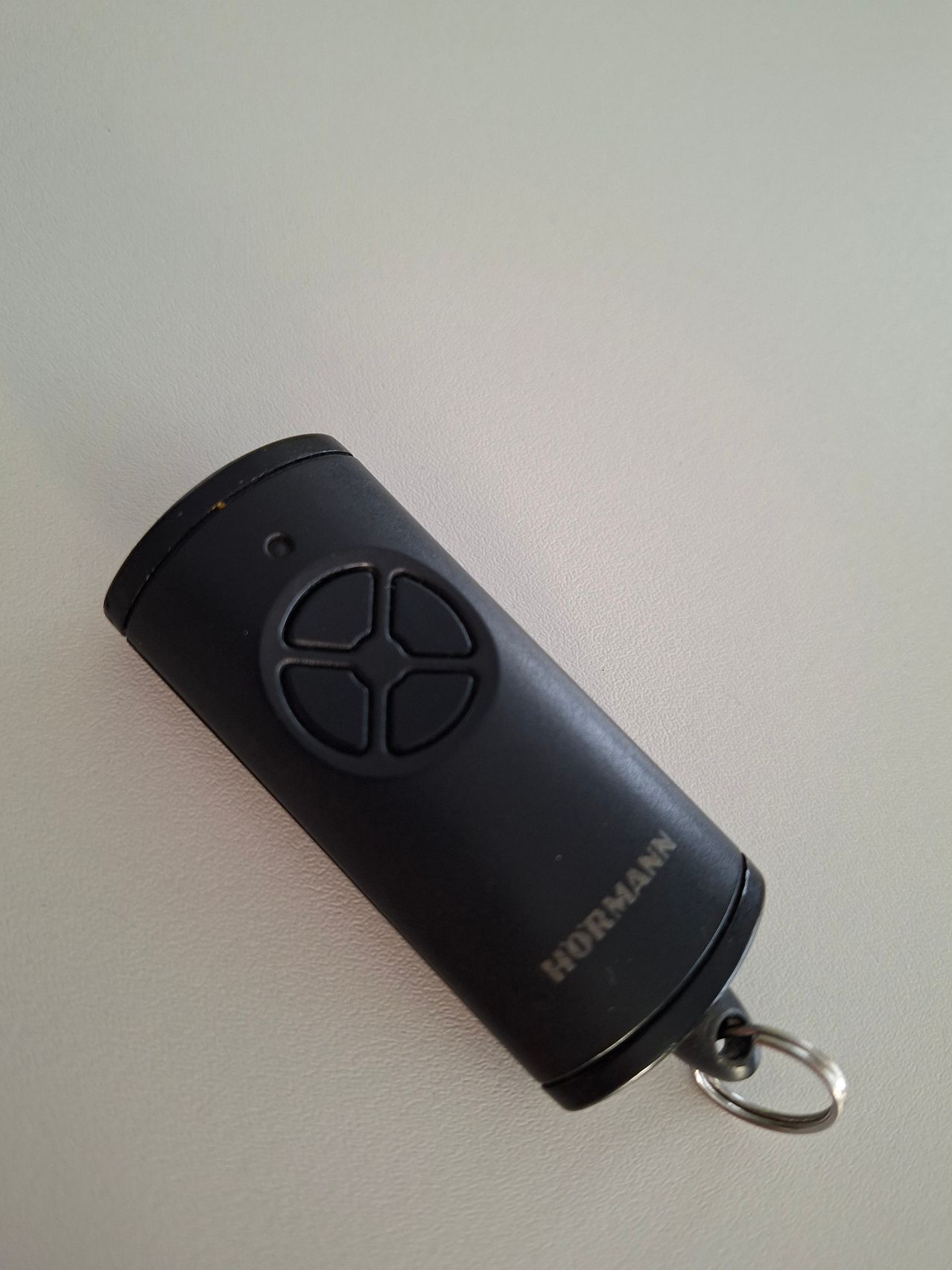 A black Hormann remote control with a circular button is placed on a white surface.