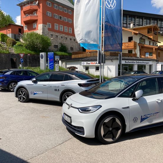 Eine Reihe von Autos parkt vor einem Gebäude mit einem Schild, das Das Welt Auto steht. Die Autos sind Volkswagens. Das Gebiet ist von Gebäuden umgeben.