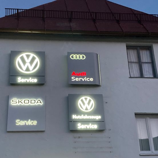 Ein Gebäude mit Schildern für Volkswagen, Audi, Skoda und Nutzfahrzeuge-Dienstleistungen. Die Schilder sind nachts beleuchtet.
