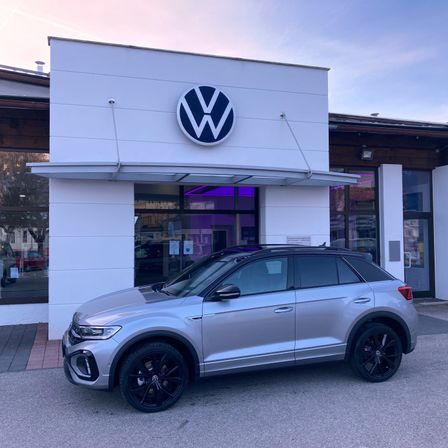 Ein silberner Volkswagen SUV steht vor einem modernen weißen Händler mit einem Volkswagen-Logo über dem Eingang.