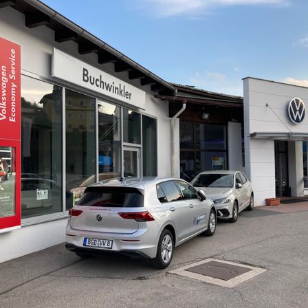 Zwei silberne Volkswagen-Autos sind vor einem Buchwinkler Volkswagen-Servicecenter bei klarem Himmel geparkt.