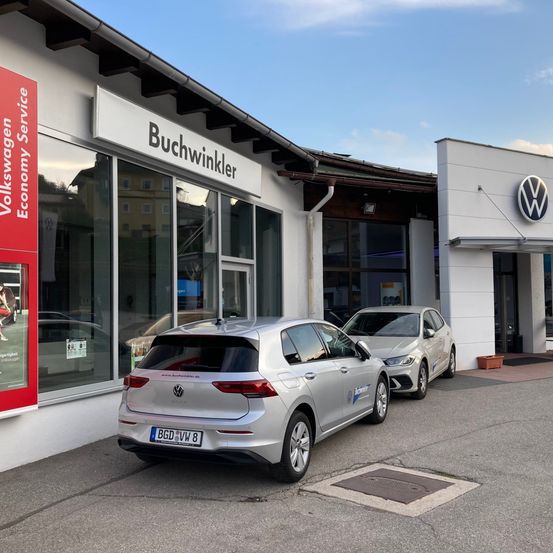 Zwei silberne Volkswagen-Autos sind vor einem Buchwinkler Volkswagen-Servicecenter bei klarem Himmel geparkt.