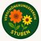 Ein rundes Emblem mit zwei Blumen, einer orange und einer gelb, auf grünem Hintergrund. Der Text lautet 'Verschönerungsverein Stubén' in Gelb.
