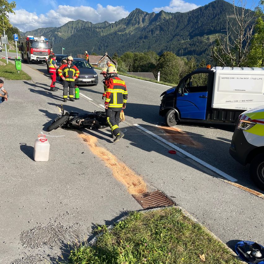 Rettungskräfte kümmern sich um einen Motorradunfall auf einer Straße mit Bergen im Hintergrund. Ein Motorrad liegt auf der Straße, und mehrere Personen in Schutzkleidung sind in der Nähe.