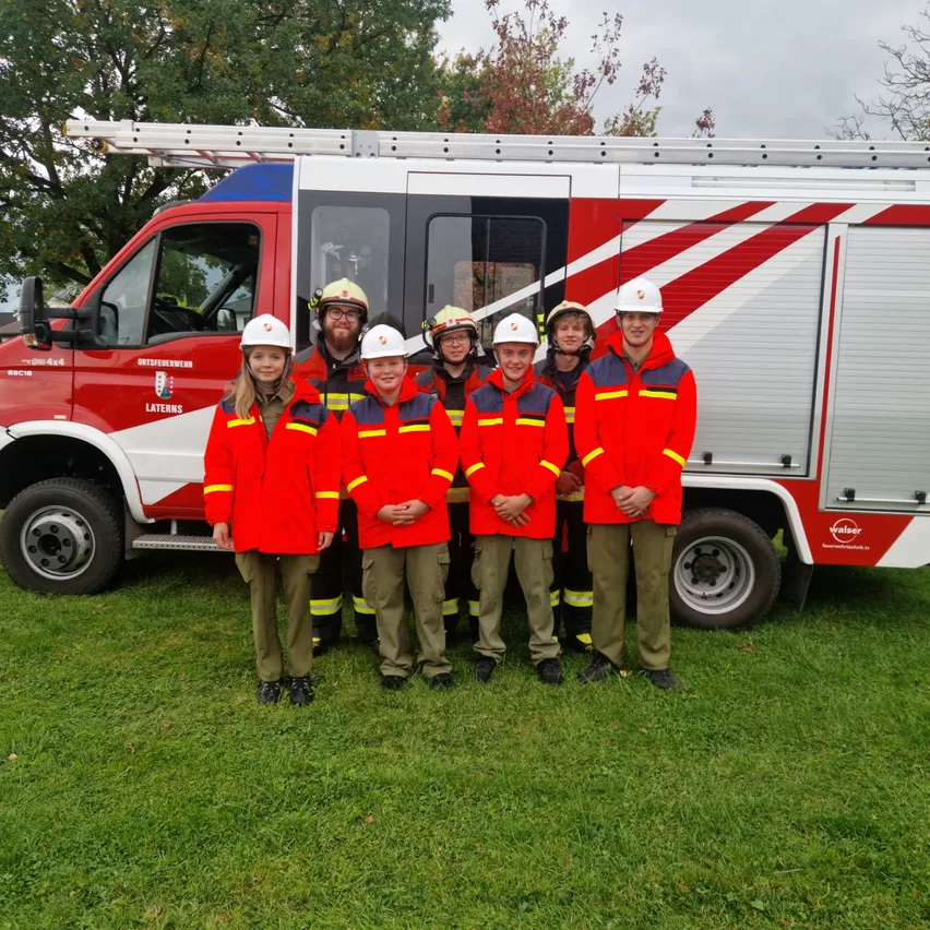Eine Gruppe von Kindern in roten Uniformen posiert für ein Foto vor einem Feuerwehrauto.