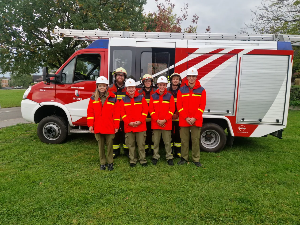 Eine Gruppe von Kindern in roten Uniformen posiert für ein Foto vor einem Feuerwehrauto.