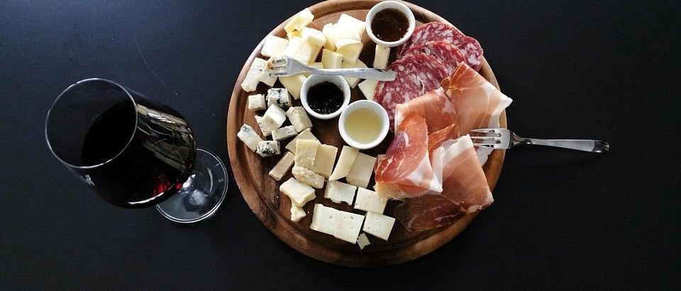 Ein Holzteller mit verschiedenen Käsesorten, Wurstwaren und Dip-Saucen, begleitet von einem Glas Rotwein.