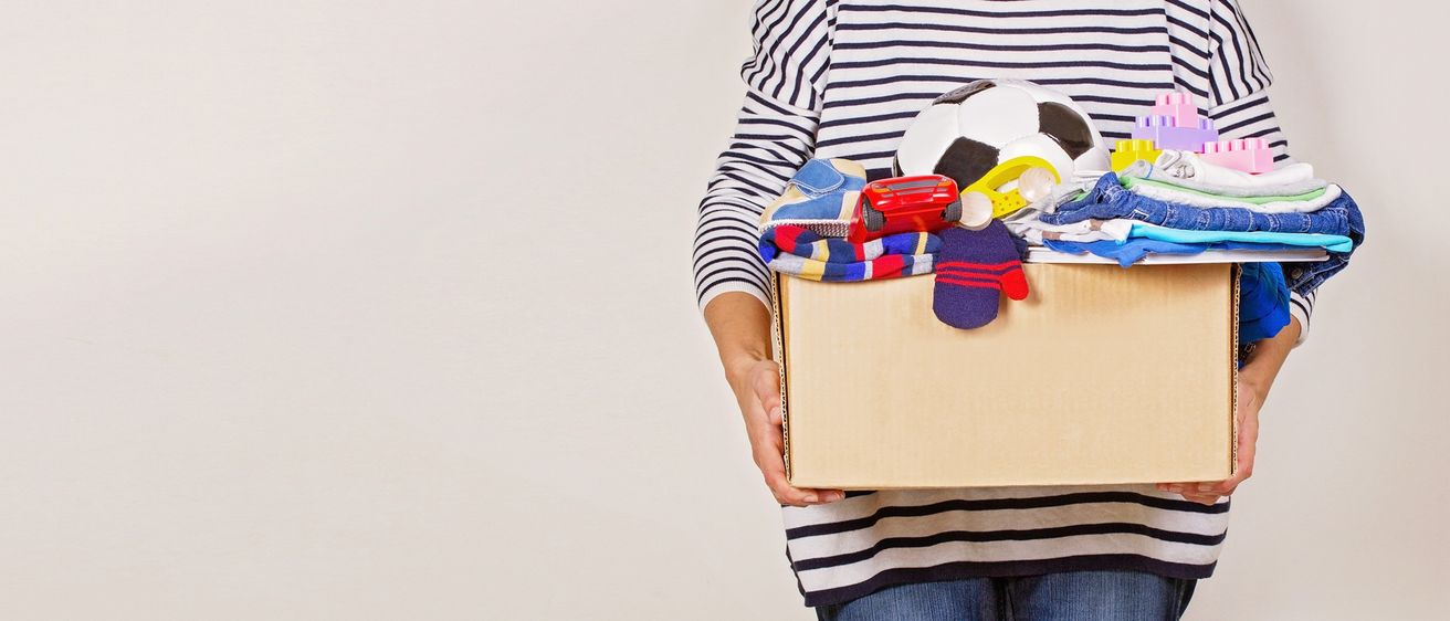 Eine Person, die eine Box mit Kinderspielzeug hält, darunter ein Fußball, Schuhe, Handschuhe und ein Auto.