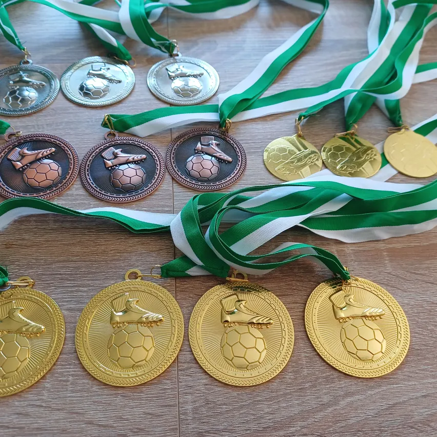 Eine Sammlung von Fußballmedaillen, einschließlich Gold, Silber und Bronze, auf einer Holzoberfläche ausgestellt. Jede Medaille zeigt einen Fußball und einen Schuh.