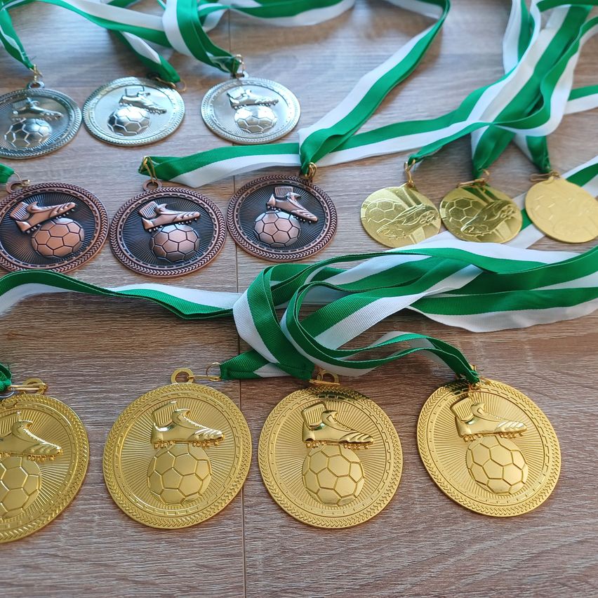 Eine Sammlung von Fußballmedaillen, einschließlich Gold, Silber und Bronze, auf einer Holzoberfläche ausgestellt. Jede Medaille zeigt einen Fußball und einen Schuh.