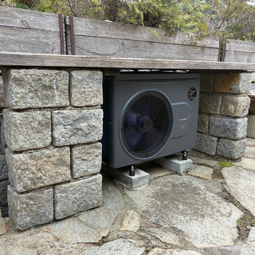 Eine graue Außenluft-Wärmepumpe ist zwischen zwei Steinsäulen in einem Garten installiert.
