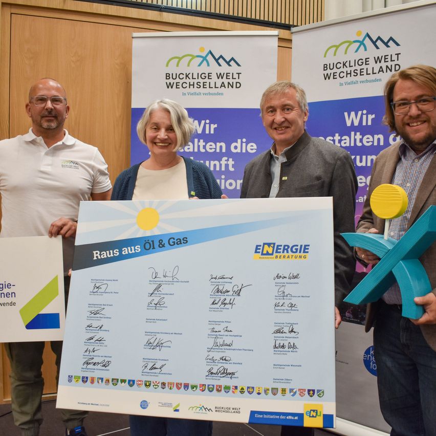 Vier Personen stehen vor einem Banner mit 'Bucklige Welt Wechselland' darauf. Die beiden Frauen und zwei Männer halten ein großes weißes Poster mit blauer und grüner Schrift. Der Mann links hält ein weißes Schild mit blauer Schrift.