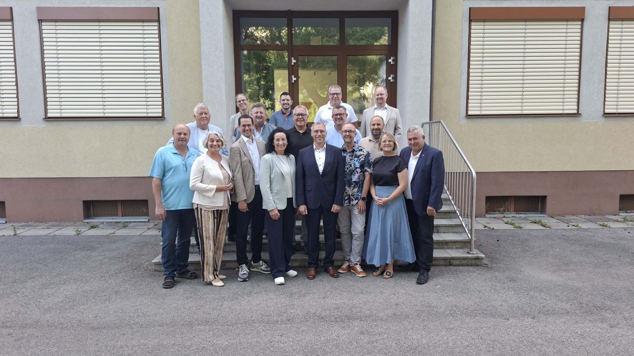 Eine Gruppe von Menschen in formeller Kleidung posiert für ein Foto vor einem Gebäude mit Glastüren und Fenstern.