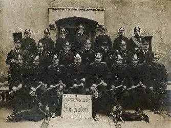 Ein altes Foto einer Gruppe uniformierter Männer, wahrscheinlich Polizeibeamte, posieren mit Schlagstöcken. Sie sitzen und stehen vor einem Gebäude.