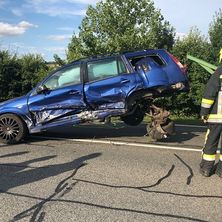 Ein blauer SUV liegt auf der Seite auf der Straße. Ein Feuerwehrmann steht neben ihm. Es gibt andere Leute in Uniform in der Nähe.