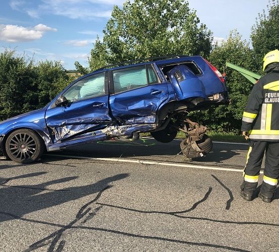 Ein blauer SUV liegt auf der Seite auf der Straße. Ein Feuerwehrmann steht neben ihm. Es gibt andere Leute in Uniform in der Nähe.