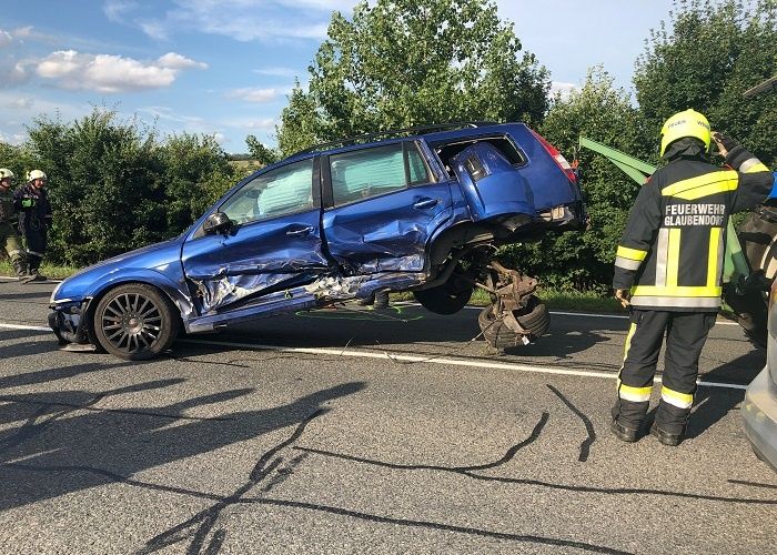 Ein blauer SUV liegt auf der Seite auf der Straße. Ein Feuerwehrmann steht neben ihm. Es gibt andere Leute in Uniform in der Nähe.