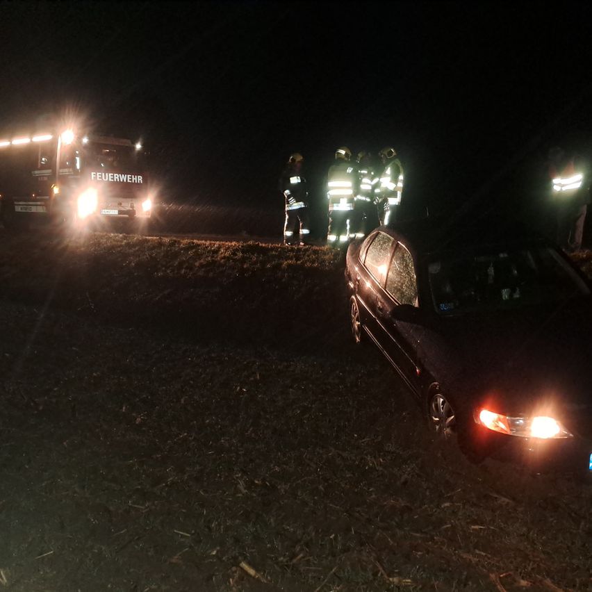 Feuerwehrleute in reflektierenden Westen stehen bei einem Unfallort in der Nacht. Ein Feuerwehrauto ist in der Nähe geparkt und beleuchtet.