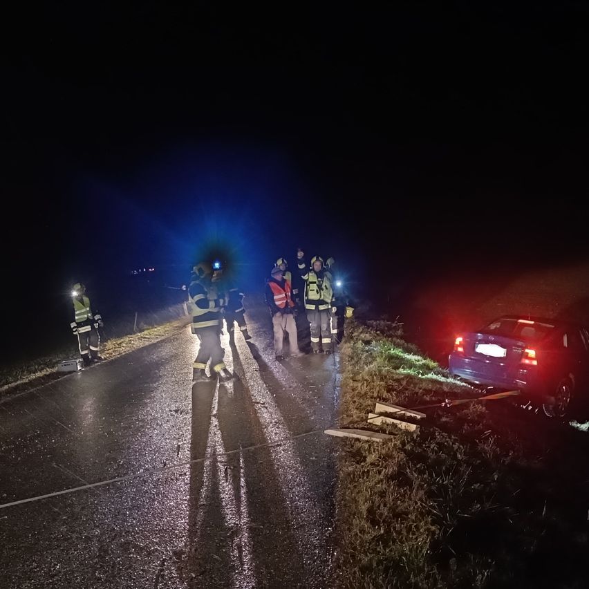 In der Nacht stehen eine Gruppe von Menschen am Straßenrand. Sie sind wahrscheinlich Feuerwehrleute. Ein Auto steht am Straßenrand. Sie reparieren wahrscheinlich das Auto.