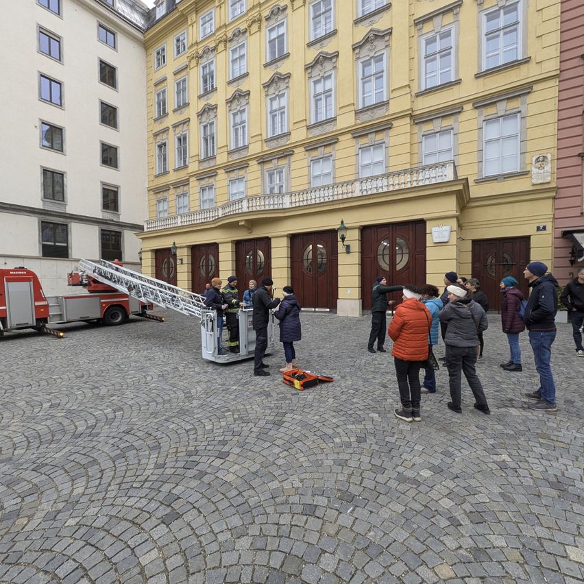 Eine Gruppe von Menschen beobachtet ein Feuerwehrauto auf einer Kopfsteinpflasterstraße vor einem historischen Gebäude.