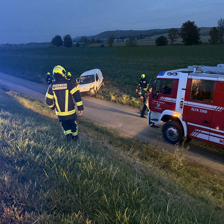 Feuerwehrleute kümmern sich um einen weißen Van am Straßenrand eines ländlichen Weges in der Dämmerung.