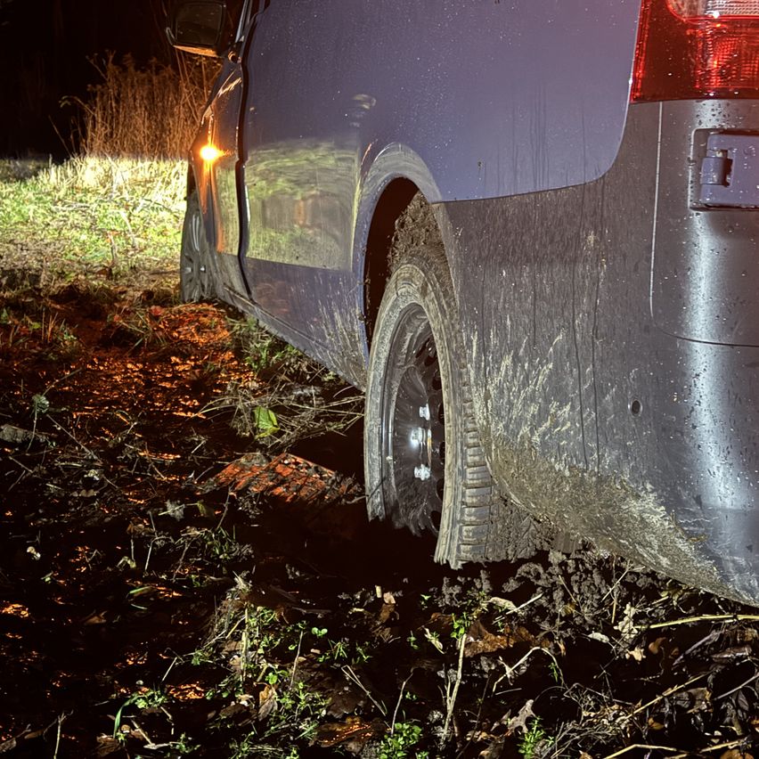 Ein dunkles Bild zeigt das Heck eines Vans, der im Schlamm feststeckt, mit Schlamm bedecktem Reifen und Stoßfänger.