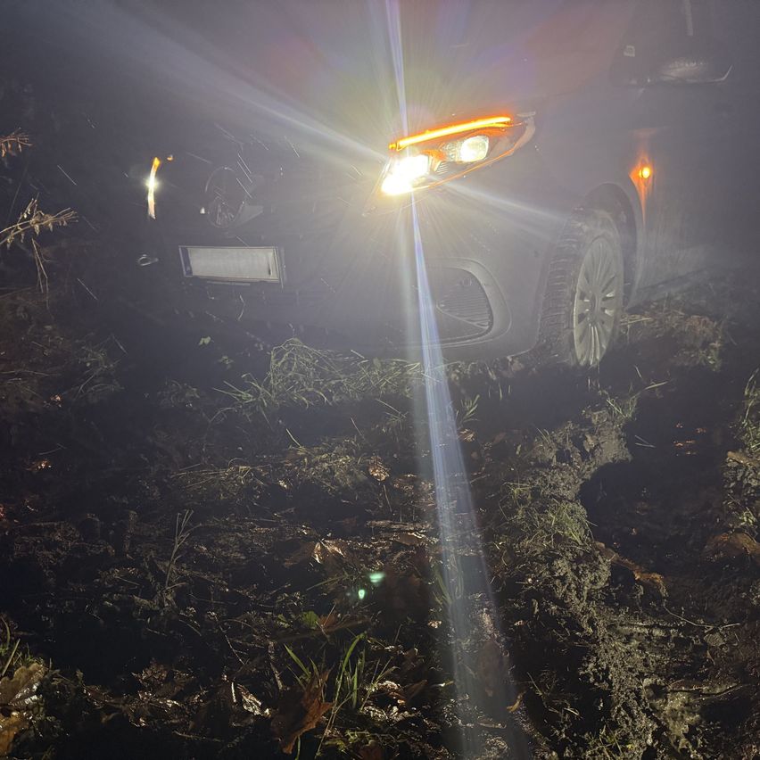 Die Scheinwerfer eines Autos sind eingeschaltet und beleuchten einen schlammigen Bereich. Das Fahrzeug scheint im Schlamm stecken geblieben zu sein.