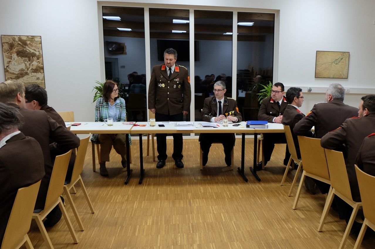 Mehrere Personen in Militäruniformen sitzen um einen Tisch in einem Besprechungsraum herum. Ein Mann steht an der Kopfseite des Tisches und spricht die Gruppe an.