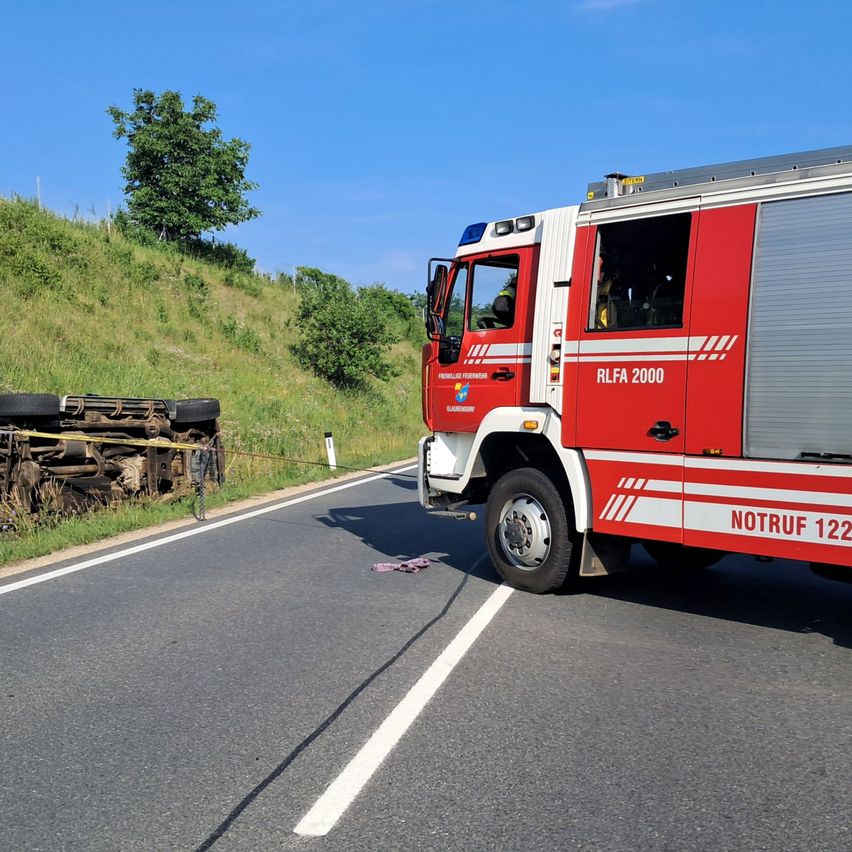 Ein roter Feuerwehrwagen mit der Nummer 122 ist am Straßenrand geparkt. Ein umgestürztes Fahrzeug ist in der Nähe, gesichert mit gelbem Klebeband.