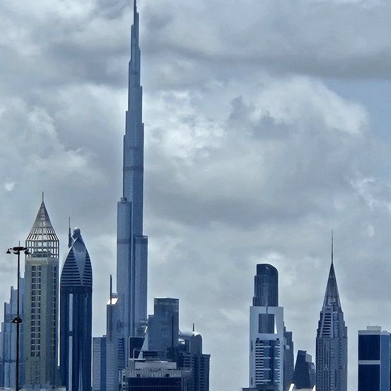 Ein Blick auf die Skyline einer Stadt mit einem markanten hohen Gebäude in der Mitte, umgeben von anderen Hochhäusern unter einem bewölkten Himmel.
