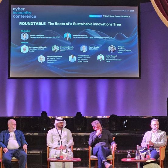 Eine Podiumsdiskussion über nachhaltige Innovationen auf einer Konferenz. Vier Männer sitzen auf Stühlen. Eine große Leinwand zeigt den Konferenztitel und die Biografien der Redner.