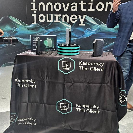 Eine Ausstellung von Kaspersky Thin Client Produkten auf einem Tisch mit schwarzer Tischdecke. Hinter dem Tisch macht ein Mann ein Foto mit einer Kamera.