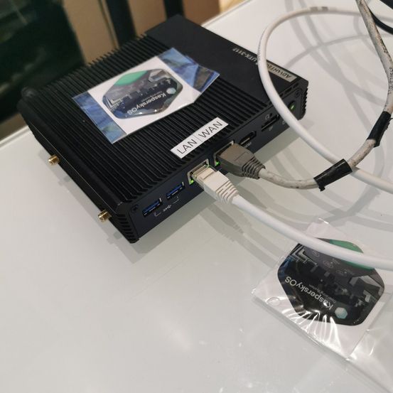 Ein schwarzes Gerät mit LAN/WAN-Etikett und mehreren Anschlüssen ist an einem Kabel auf einer weißen Oberfläche angeschlossen.
